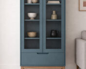 ארון ויטרינה דגם סקיי בצבע כחול עם דלתות זכוכית, מדפים פנימיים, מגירה תחתונה ורגלי עץ אלון מלא בגוון טבעי